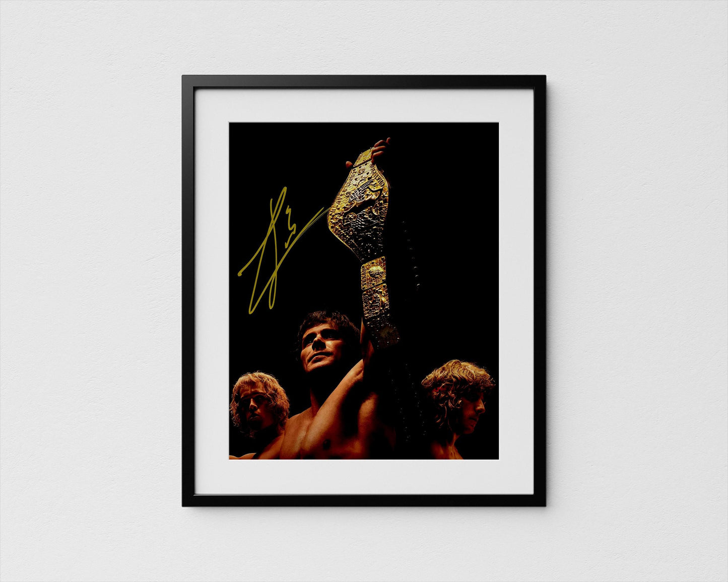 A framed photograph of a person holding a large golden trophy, with two other people in the background. Iron Claw with Zac Efron