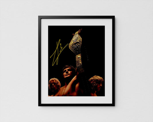 A framed photograph of a person holding a large golden trophy, with two other people in the background. Iron Claw with Zac Efron