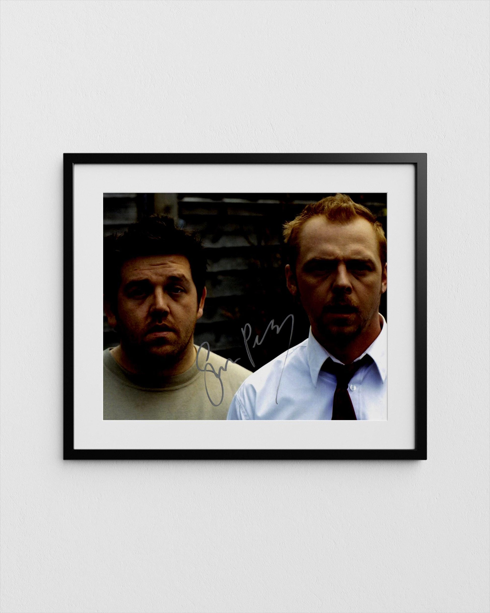 The image is a framed photograph of two men, one wearing a tie and the other in a casual shirt, both looking directly at the camera.