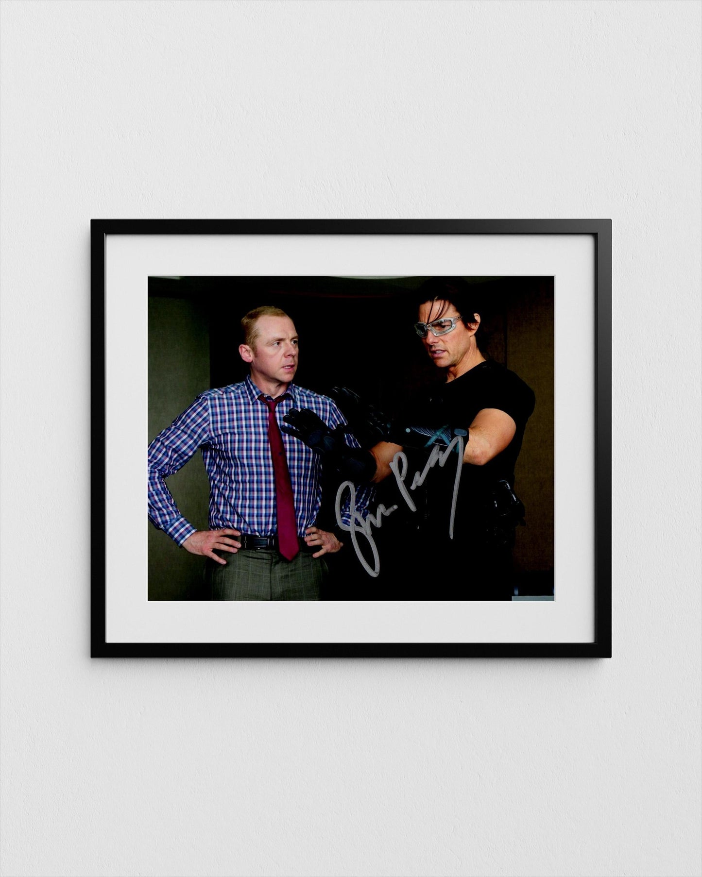tom cruise and simon pegg, one wearing a blue plaid shirt and the other wearing a black shirt, posing together in a framed photograph.