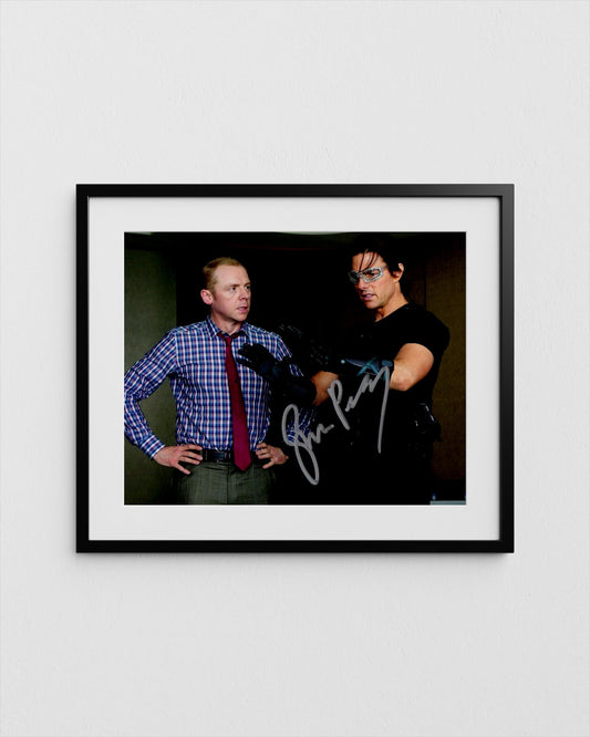 tom cruise and simon pegg, one wearing a blue plaid shirt and the other wearing a black shirt, posing together in a framed photograph.