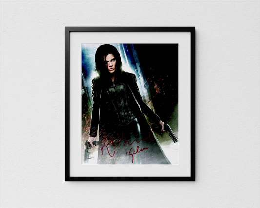 A framed poster featuring a woman with long dark hair, wearing a black outfit and holding a gun, against a dark background with a bright light source.